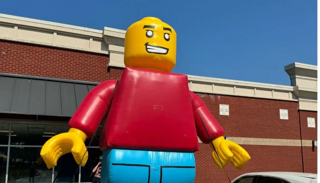 Large inflatable figure of a LEGO character outside a brick building under a clear blue sky