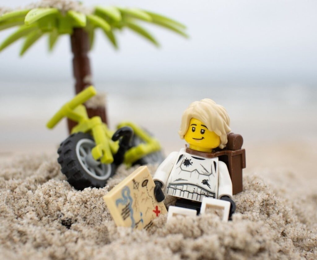LEGO mini-figure on a sandy beach holding a treasure map, next to a palm tree and a yellow bicycle