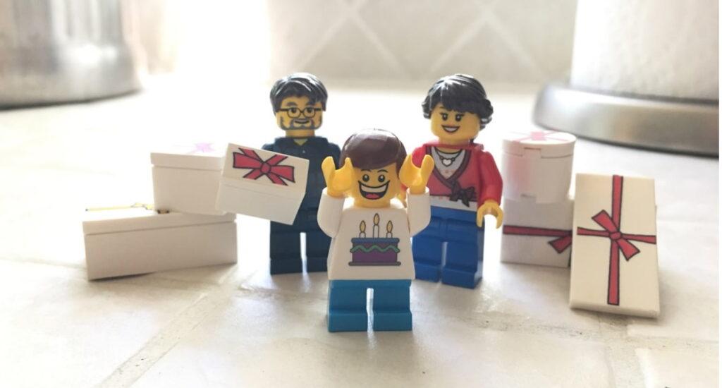 LEGO mini-figures of a family celebrating with a child holding up hands in excitement, surrounded by several gift boxes.