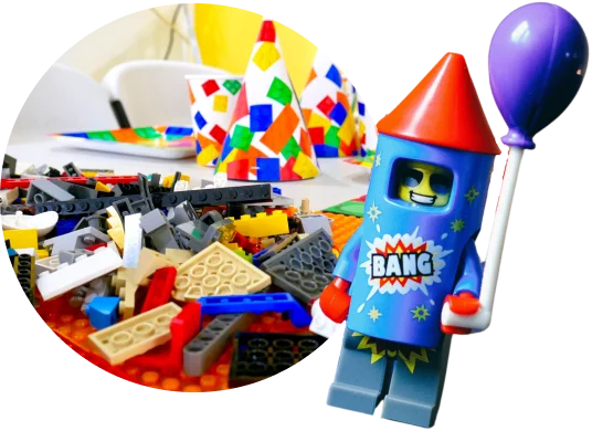 LEGO mini-figure dressed as a rocket holding a balloon, with a pile of LEGO bricks and colorful party hats in the background