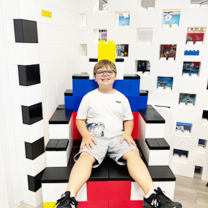 Two children racing LEGO® cars down a derby race track