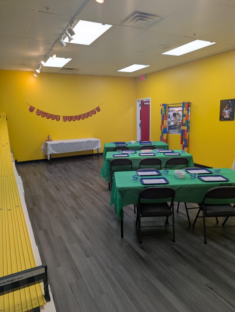 Birthday party room setup at Bricks & MiniFigs Schaumburg with Lego® building, tables, derby cars, and kids activities