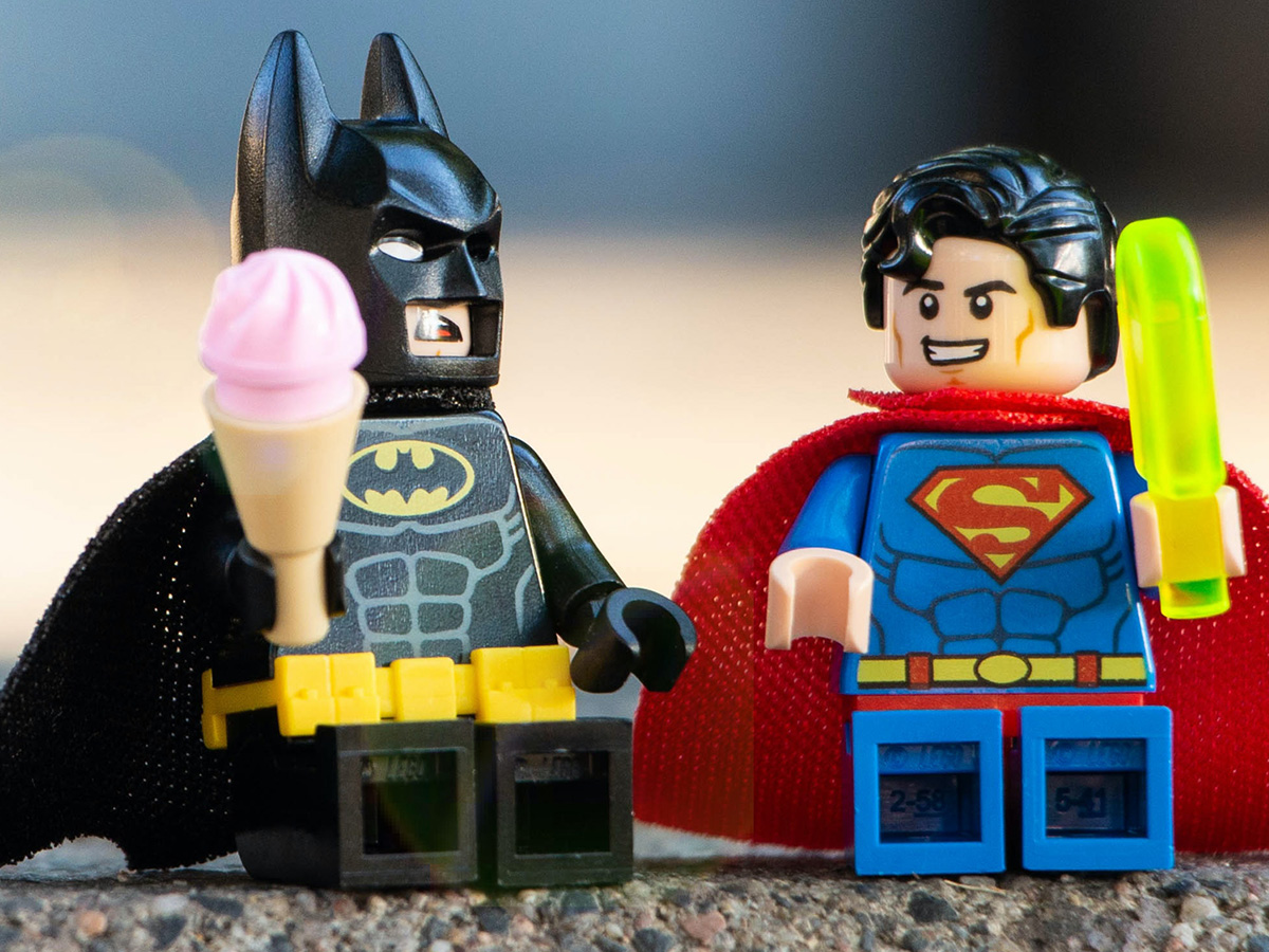 Two LEGO® minifigs of batman and superman sitting next to each other.