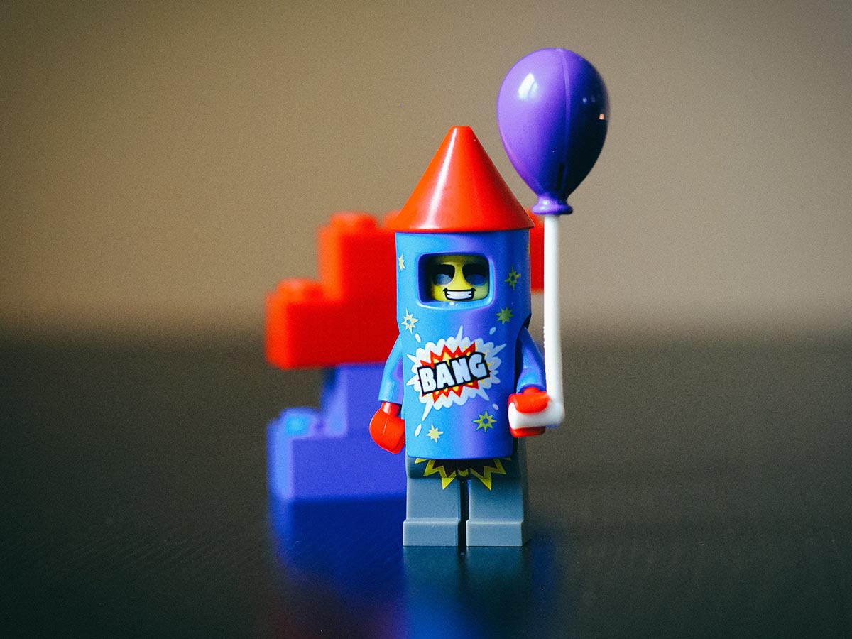 Blue and red Firecracker LEGO® minigure holding a purple balloon.