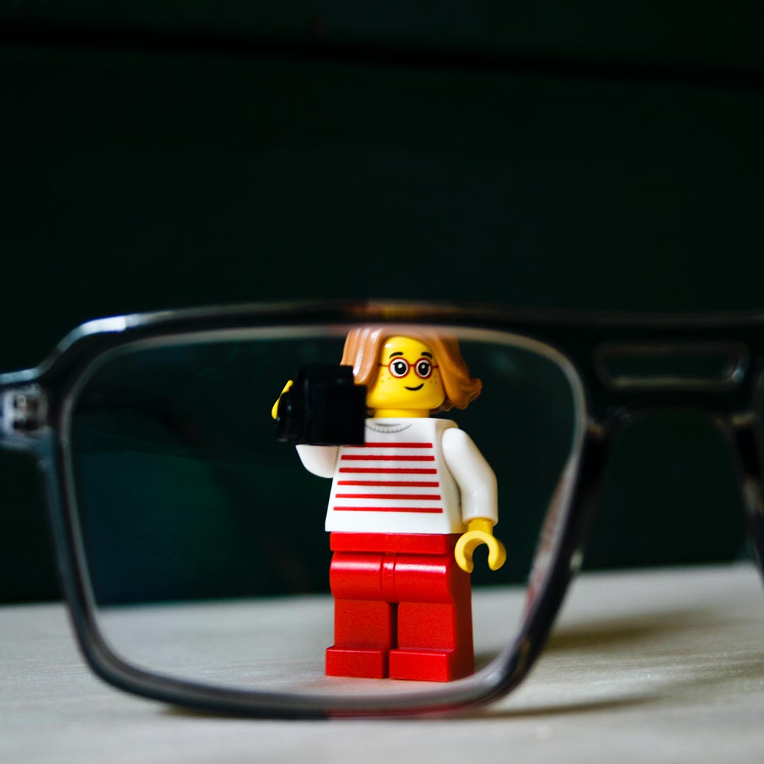 Photographer Lego figurine next to a pair of eyeglasses