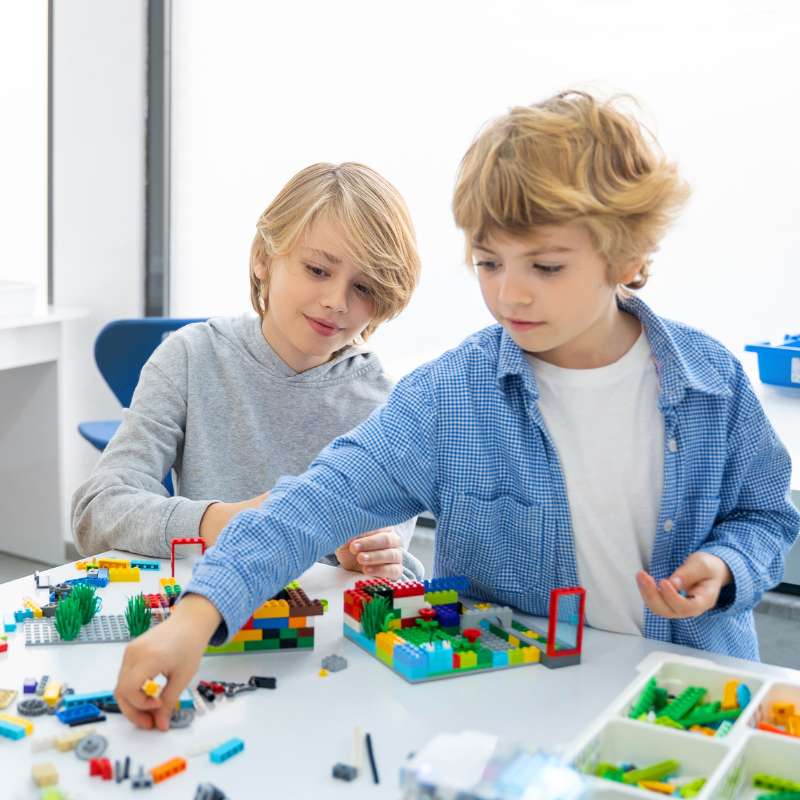 Two boys building with LEGO® bricks on a white table in a brightly lit, white room.