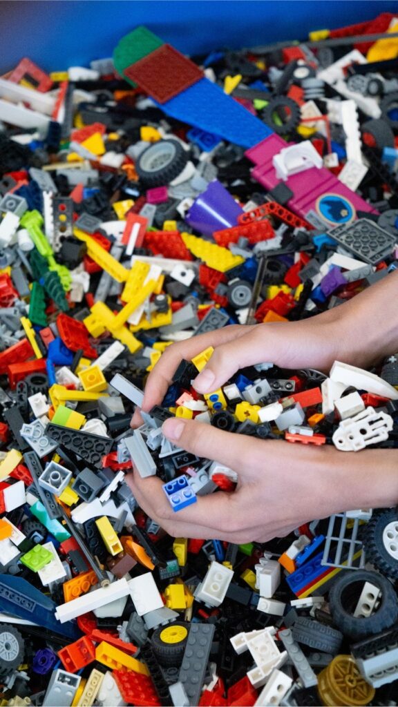 Hands building a small LEGO® build above a table filled with bulk LEGO pieces