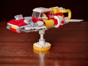 A flying car MOC LEGO® build made from red, yellow, white, and gray bricks on a wood table
