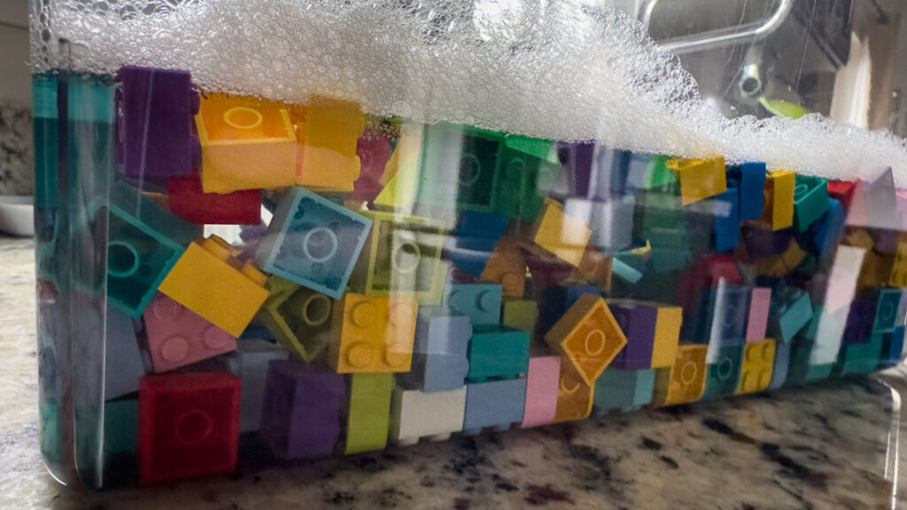 Bulk LEGO bricks of different colors soaking in a large tub of soapy water.