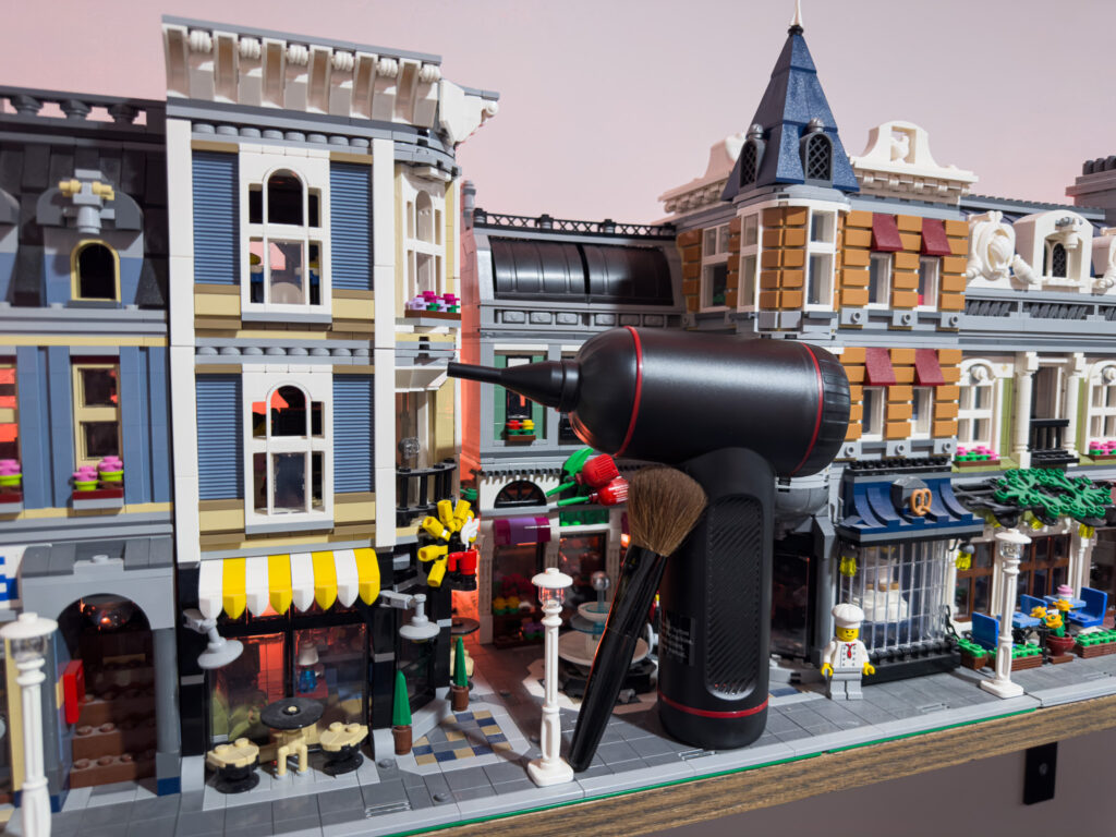 A makeup brush leaning against an electronic duster in front of a LEGO neighborhood build.