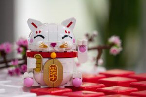 A waving, white Lucky Cat LEGO set with a Cherry Blossom set in the background.