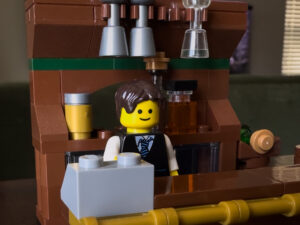 A LEGO minifig bartender standing at a bar made of bricks.