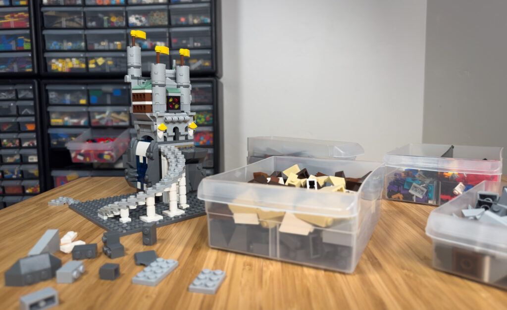 A custom LEGO® castle being built next to plastic bins of color-sorted LEGO bricks in order to get started building LEGO MOCs