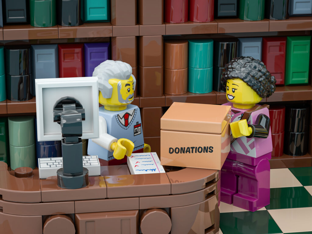 A LEGO® minifigure bringing a box of donations to another minifig in a library made of LEGO bricks.