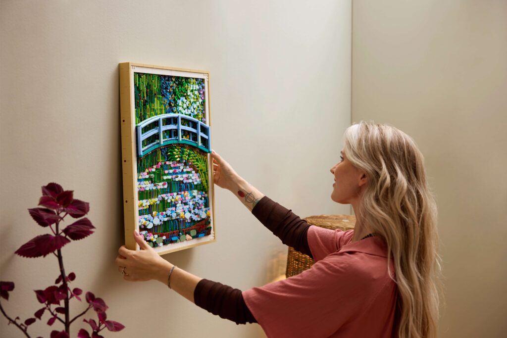 A woman hanging the Claude Monet – Bridge over a Pond of Water Lilies LEGO® set on the wall.