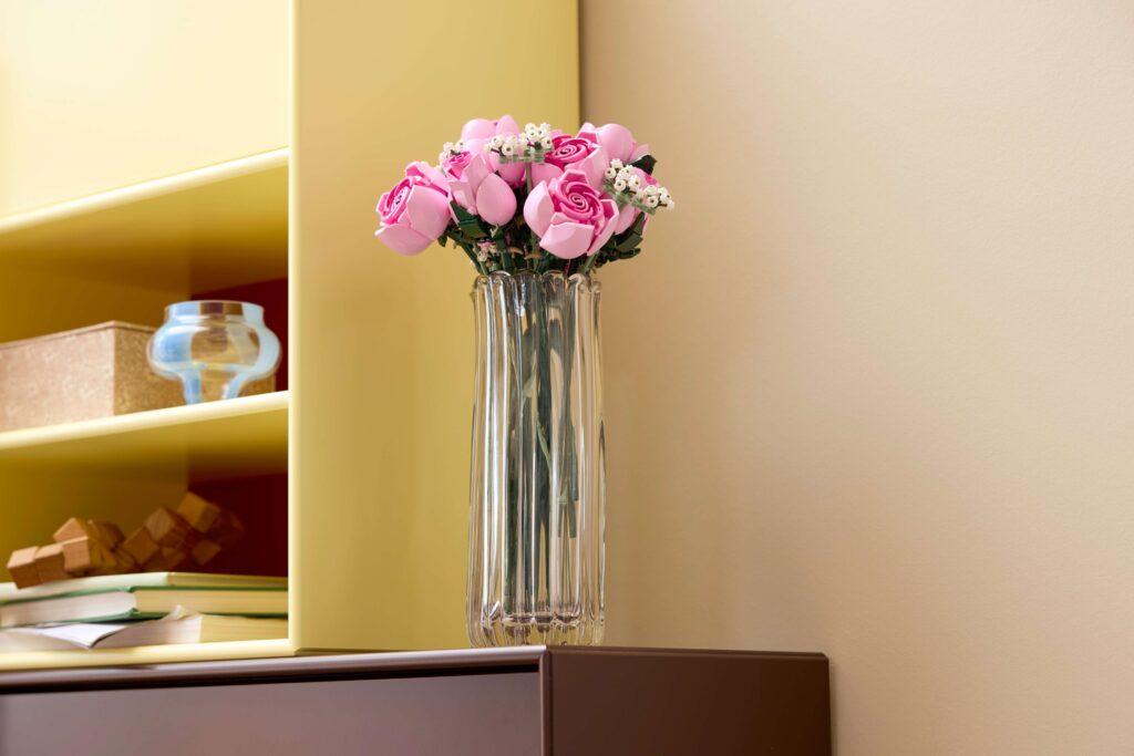 The Bouquet of Pink Roses LEGO® set in a glass vase on a shelf.